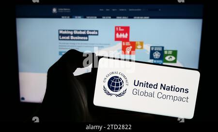 Persona che possiede uno smartphone con il logo del Patto delle Nazioni Unite Global Compact davanti al sito Web. Concentrarsi sul display del telefono. Foto Stock