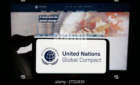 Persona in possesso di un cellulare con il logo del Patto delle Nazioni Unite Global Compact davanti alla pagina web. Concentrarsi sul display del telefono. Foto Stock