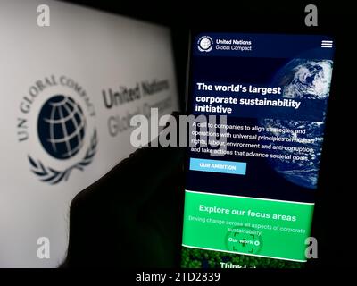 Persona in possesso di cellulare con pagina Web del Patto delle Nazioni Unite Global Compact davanti al logo. Concentrarsi sul centro del display del telefono. Foto Stock