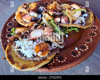 Delizioso piatto di Sopes e tostadas di pesce che sono una tortilla fritta con fagioli, gamberi e polpo in cima Foto Stock