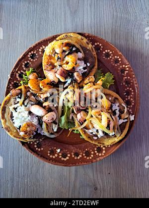 Delizioso piatto di Sopes e tostadas di pesce che sono una tortilla fritta con fagioli, gamberi e polpo in cima Foto Stock