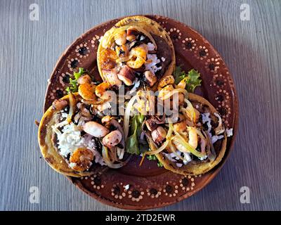 Delizioso piatto di Sopes e tostadas di pesce che sono una tortilla fritta con fagioli, gamberi e polpo in cima Foto Stock
