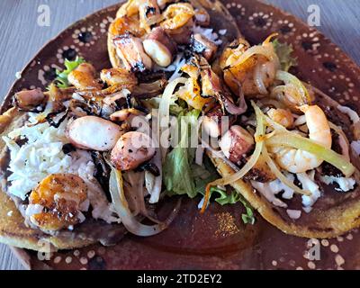 Delizioso piatto di Sopes e tostadas di pesce che sono una tortilla fritta con fagioli, gamberi e polpo in cima Foto Stock