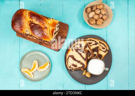 Cozonac, tradizionale pane dolce rumeno con ripieno di noci, a fette, con un bicchiere di latte su tavole di legno blu Foto Stock