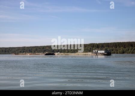 Un rimorchiatore spinge chiatte combinate caricate di sabbia lungo il Danubio Foto Stock