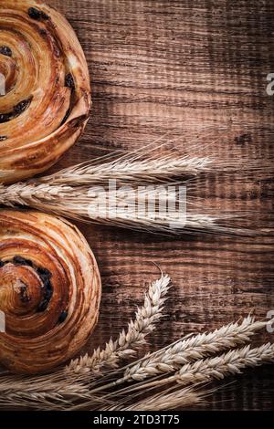 Orecchie di grano maturo panini appena sfornati con uva passa su tavola di legno di quercia e concetto di cibo e bevande Foto Stock