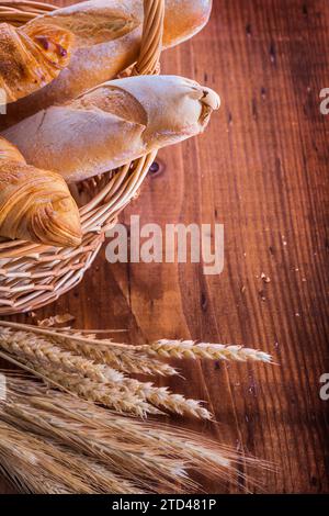 Baguette e croissant in cesto di vimini orecchie di segale di grano su tavola di legno vintage concetto di cibo e bevande Foto Stock