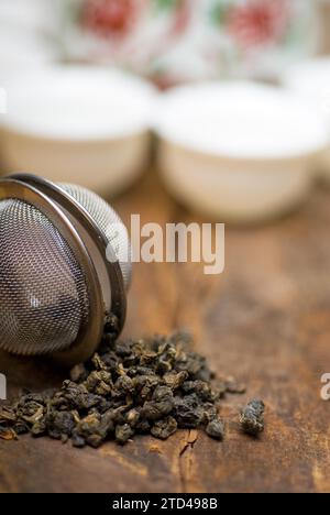 Set da tè cinese verde secco, con primo piano del filtro, tazze e teiera sullo sfondo su un vecchio asse di legno, fotografia gastronomica Foto Stock