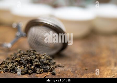 Set da tè cinese verde secco, con primo piano del filtro, tazze e teiera sullo sfondo su un vecchio asse di legno, fotografia gastronomica Foto Stock