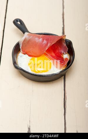Uovo fritto al sole con prosciutto italiano affumicato in speck tirolese su una padella Foto Stock