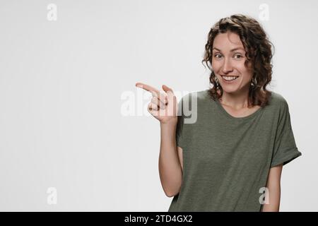 La donna allegra indica con il dito indice uno spazio vuoto per la copia, mostra il posto per la tua pubblicità o il testo promozionale. la ragazza mostra qualcosa di fantastico, isolata su sfondo bianco. Concetto sorprendente. Foto Stock