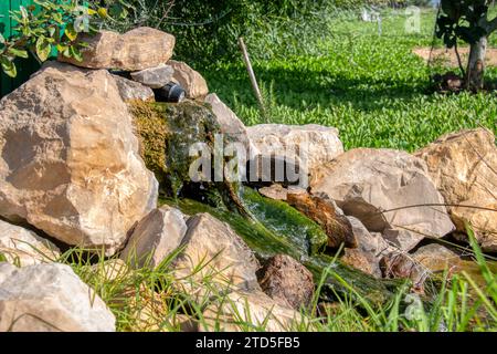 Fontana con rocce con verdigris da cui scorre l'acqua che decora un giardino. Foto Stock