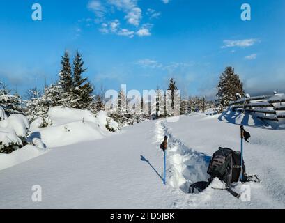 Inverno remoto villaggio alpino periferia, innevate derive sul bordo di montagna abete foresta. Zaino turistico su un percorso escursionistico appena trodden. Foto Stock