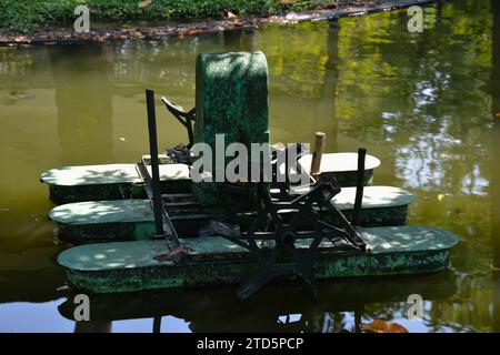 Una turbina ad acqua in stile thailandese che lavora in uno stagno naturale accanto a un campo di riso nella campagna della Thailandia Foto Stock