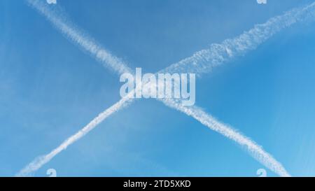 Aeromobile contrails crossing e formando una X in un cielo blu Foto Stock