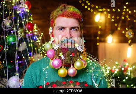 Capodanno e festeggiamenti di Natale. Uomo barbuto con palle di Natale in barba. Barbiere per Natale e Capodanno. Uomo sorridente con barba decorata Foto Stock