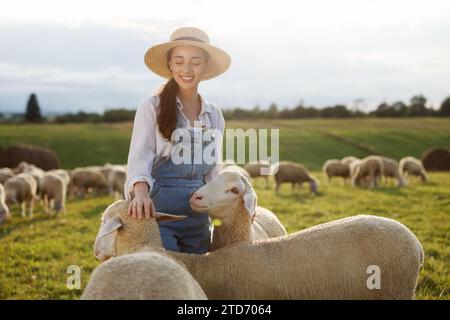 Donna sorridente che accarezza pecore al pascolo in fattoria Foto Stock