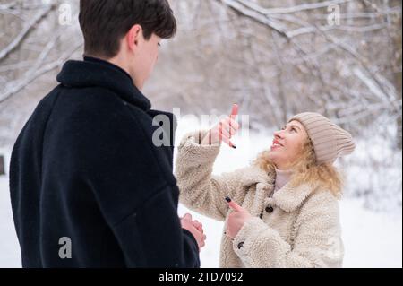 Una giovane coppia cammina in inverno nella foresta. Il ragazzo sordo e una ragazza comunicano usando i gesti all'aperto. Foto Stock