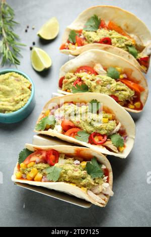 Deliziosi tacos con guacamole, carne e verdure serviti su un tavolo grigio Foto Stock