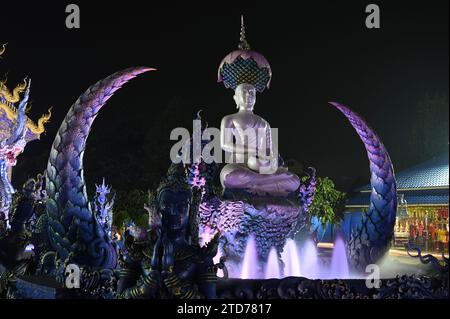 Scena notturna di Phra Upakut è una statua bianca perla posta al centro di una fontana. Di fronte alla cappella del tempio Wat Rong Suea Ten. Foto Stock