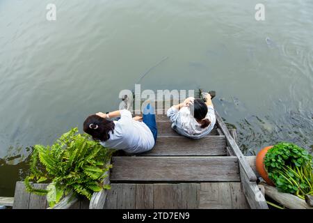 Nonthaburi, Thailandia - 29 ottobre 2023: Vista dall'alto delle persone sedute e che danno da mangiare ai pesci sulle scale del molo nel distretto di Bang Yai nella provincia di Nonthaburi, Foto Stock