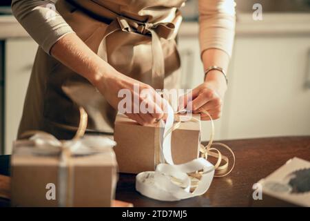 Primo piano le mani delle donne legano il nastro sulla scatola per l'ordine del cliente. Pasticceria e torta in cucina. Imprenditore di piccole imprese e cibo Foto Stock