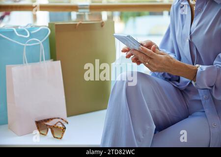 Donna matura ed elegante dopo aver fatto acquisti chiacchierando sui social media in smartphone Foto Stock