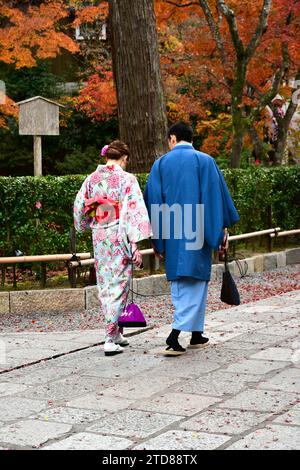 Coppia giapponese in abito tradizionale che cammina lungo la passerella con lo sfondo dei colori delle foglie autunnali. Foto Stock