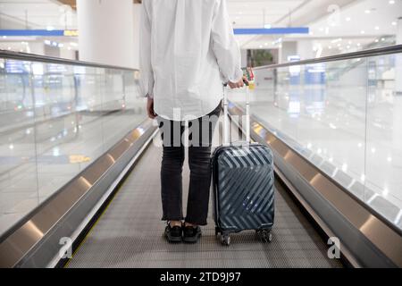 Vista posteriore di una donna che si muove usando una scala mobile all'aeroporto Foto Stock