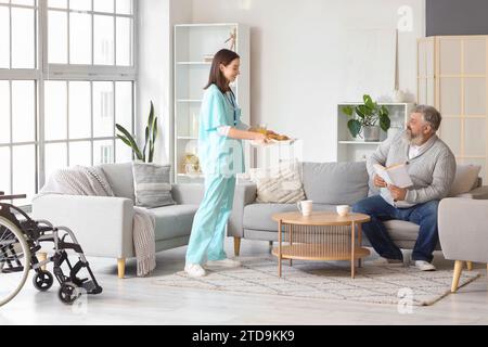 Infermiera che porta la colazione all'uomo maturo a casa Foto Stock