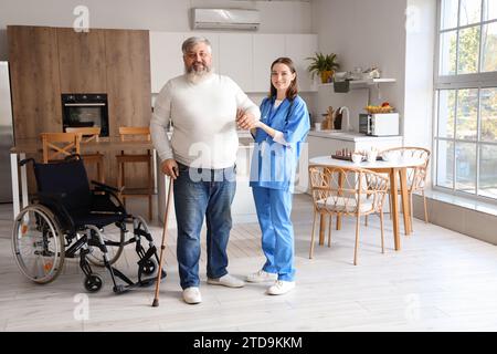 Infermiera che aiuta l'uomo maturo con il bastone da passeggio in cucina Foto Stock