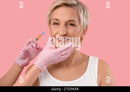 Bella donna matura che riceve l'iniezione su sfondo rosa, primo piano Foto Stock