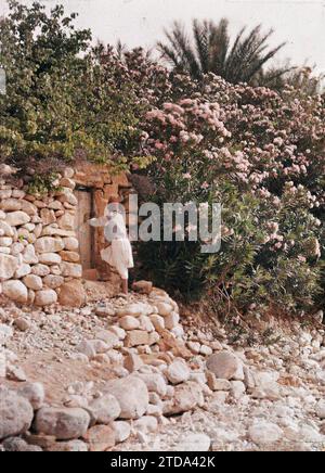 El Kantara, Algeria Un giovane ragazzo vicino al cancello di un giardino, esseri umani, Habitat, architettura, natura, ambiente, bambino, fiore, porta, Parco, giardino, vegetazione, botanica, El Kantara, oleandri, El Kantara, 01/01/1911 - 31/12/1911, 01/01/1910 - 31/12/1910, 01/01/1909 - 31/12/1909, Gervais-Courtellemont, Jules, 1909 ou 1910 - Algérie, Tunisie - Jules Gervais-Courtellemont et Souvieux, Autochrome, Photo, Glass, Autochrome, foto, verticale, dimensioni 9 x 12 cm Foto Stock