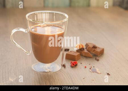 Latte al cioccolato in vetro e pezzi di cioccolato su tavola di legno Foto Stock