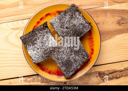 Tre pezzi di classico brownie al cioccolato con piattino in ceramica su tavolo in legno, macro, vista dall'alto. Foto Stock