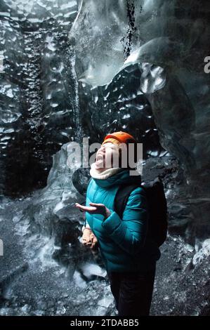 Donna che beve acqua di scolo che gocciola da un ghiacciaio in Islanda Foto Stock
