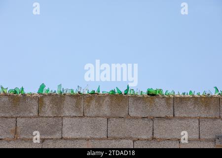 Vetro verde rotto in cima alla parete con cielo blu Foto Stock