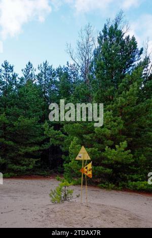 Un segnale di avvertimento giallo nel mezzo di una foresta. Segnale di inquinamento da radiazioni vicino agli alberi nella zona di esclusione di Chernobyl. Foto Stock