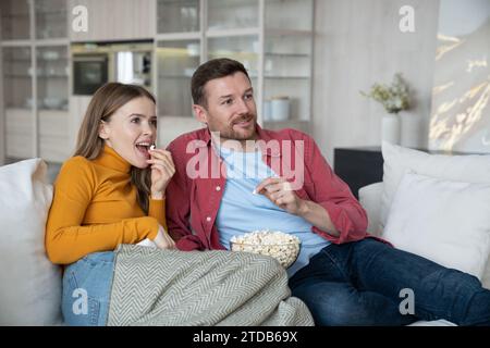 Spensierata moglie e marito trascorrono passatempo insieme, rilassandosi a casa, guardando la TV, mangiando popcorn Foto Stock
