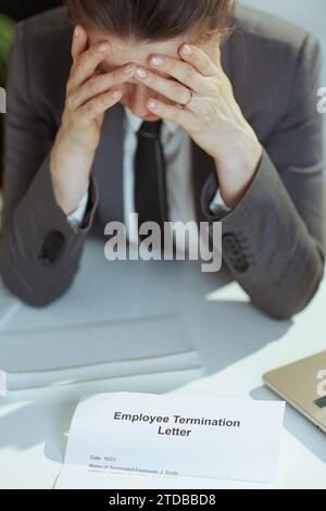 Nuovo lavoro. Primo piano su una moderna lavoratrice di 40 anni in un moderno ufficio verde in una tuta aziendale grigia con lettera di licenziamento dei dipendenti. Foto Stock