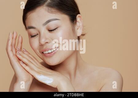 Ritratto di una giovane donna con crema per le mani su sfondo beige. Foto Stock