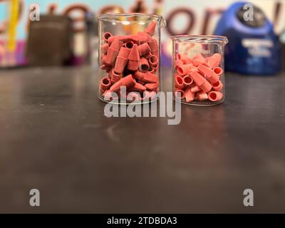 Tappi rosa per gomma a matita in un becher da laboratorio in vetro trasparente su un tavolo nero. Foto Stock