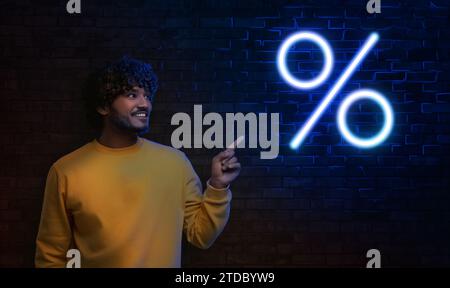 Offerta scontata. Uomo felice che indica il simbolo della percentuale di neon sul muro di mattoni al buio, design dello striscione Foto Stock