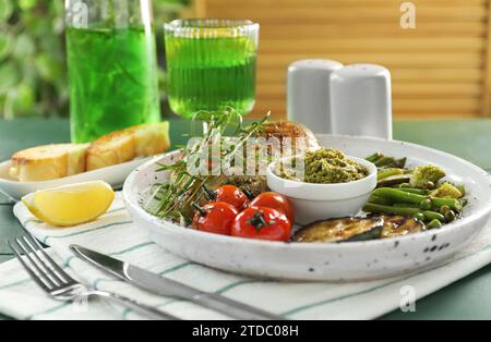 Gustoso pollo, verdure con dragoncello e pesto serviti su un tavolo di legno verde Foto Stock