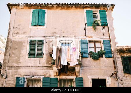 La lavanderia colorata si asciuga sulla linea del balcone di un'antica casa in pietra con persiane di legno verdi Foto Stock