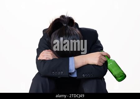 Una donna disperata che tiene in mano una bottiglia di alcol con la testa in basso davanti a uno sfondo bianco Foto Stock