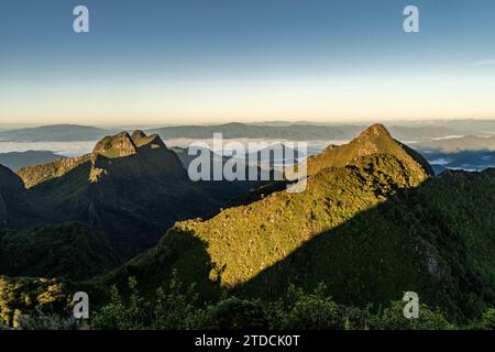 Vista dalla cima di Doi Luang Chiang Dao durante un'alba mattutina con alberi e arbusti in primo piano e splendide catene montuose sullo sfondo Foto Stock