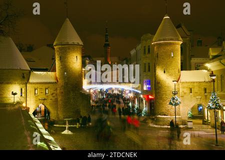 Torri di pietra della porta Viru con centinaia di acquirenti e folle festose che camminano (movimento sfocato) verso il mercato di Natale nella città vecchia di Tallinn, Estonia Foto Stock