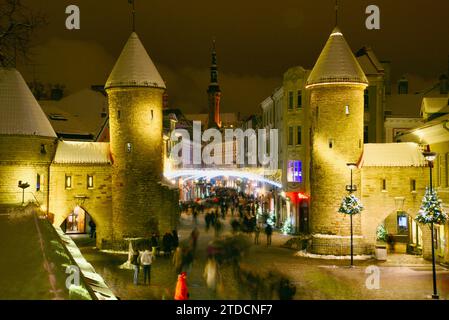 Torri di pietra della porta Viru con centinaia di acquirenti e folle festose che camminano (movimento sfocato) verso il mercato di Natale nella città vecchia di Tallinn, Estonia Foto Stock