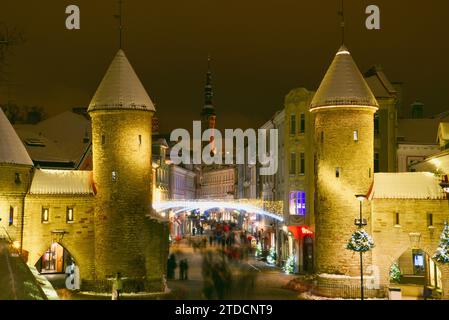 Torri di pietra della porta Viru con centinaia di acquirenti e folle festose che camminano (movimento sfocato) verso il mercato di Natale nella città vecchia di Tallinn, Estonia Foto Stock